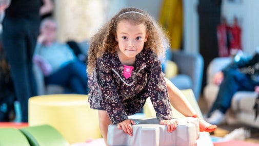 A little girl climbing over a piece of soft play looking towards the camera